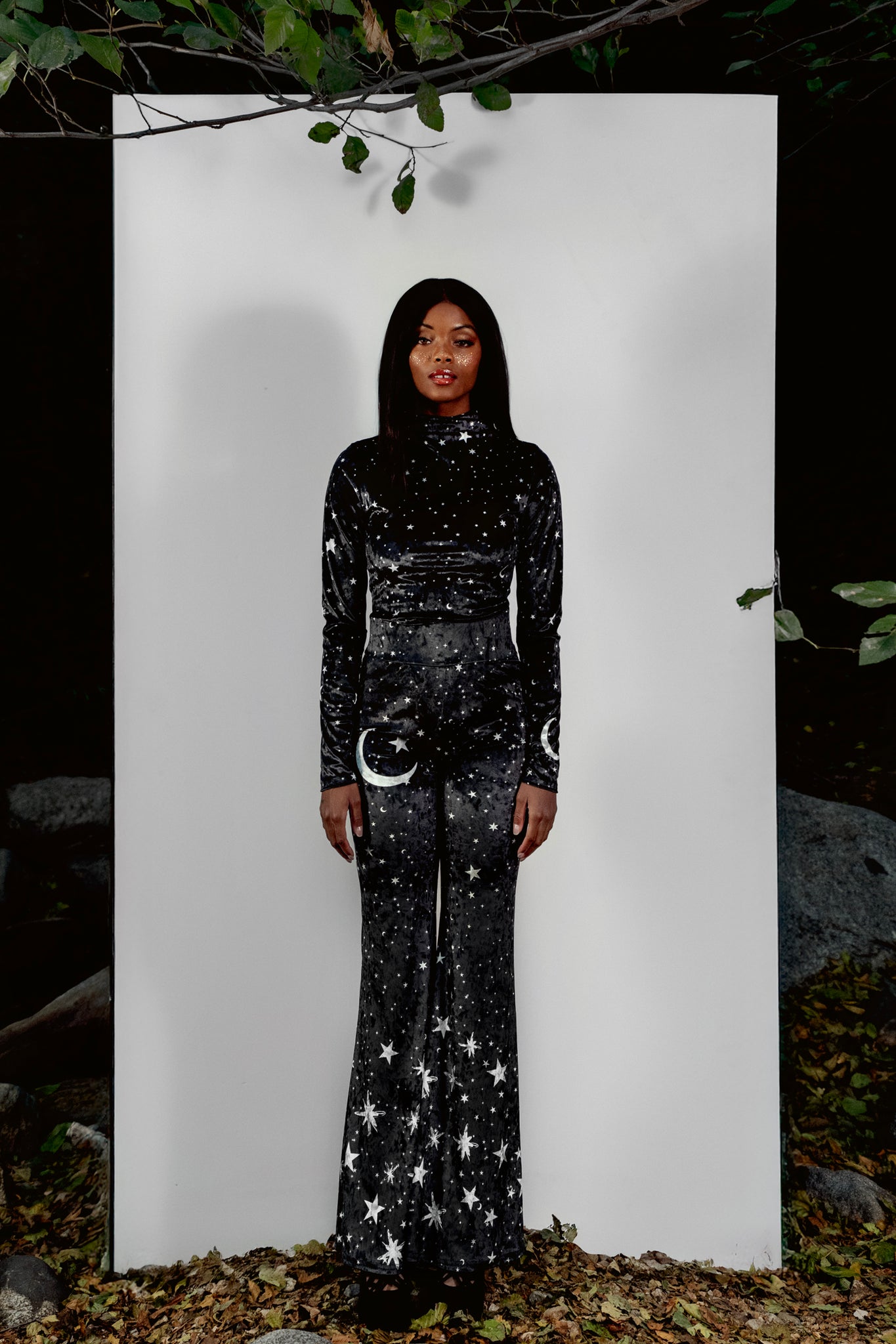 Person wearing black bell pants with star and moon designs against a white background.