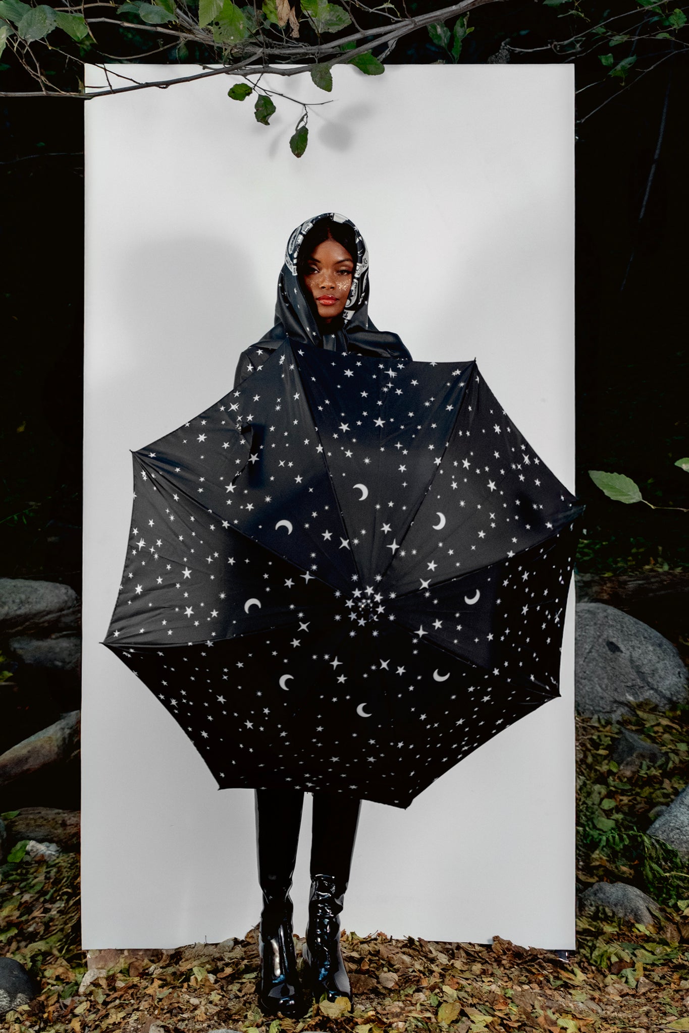 Person holding a black umbrella with star and moon pattern against a white background
