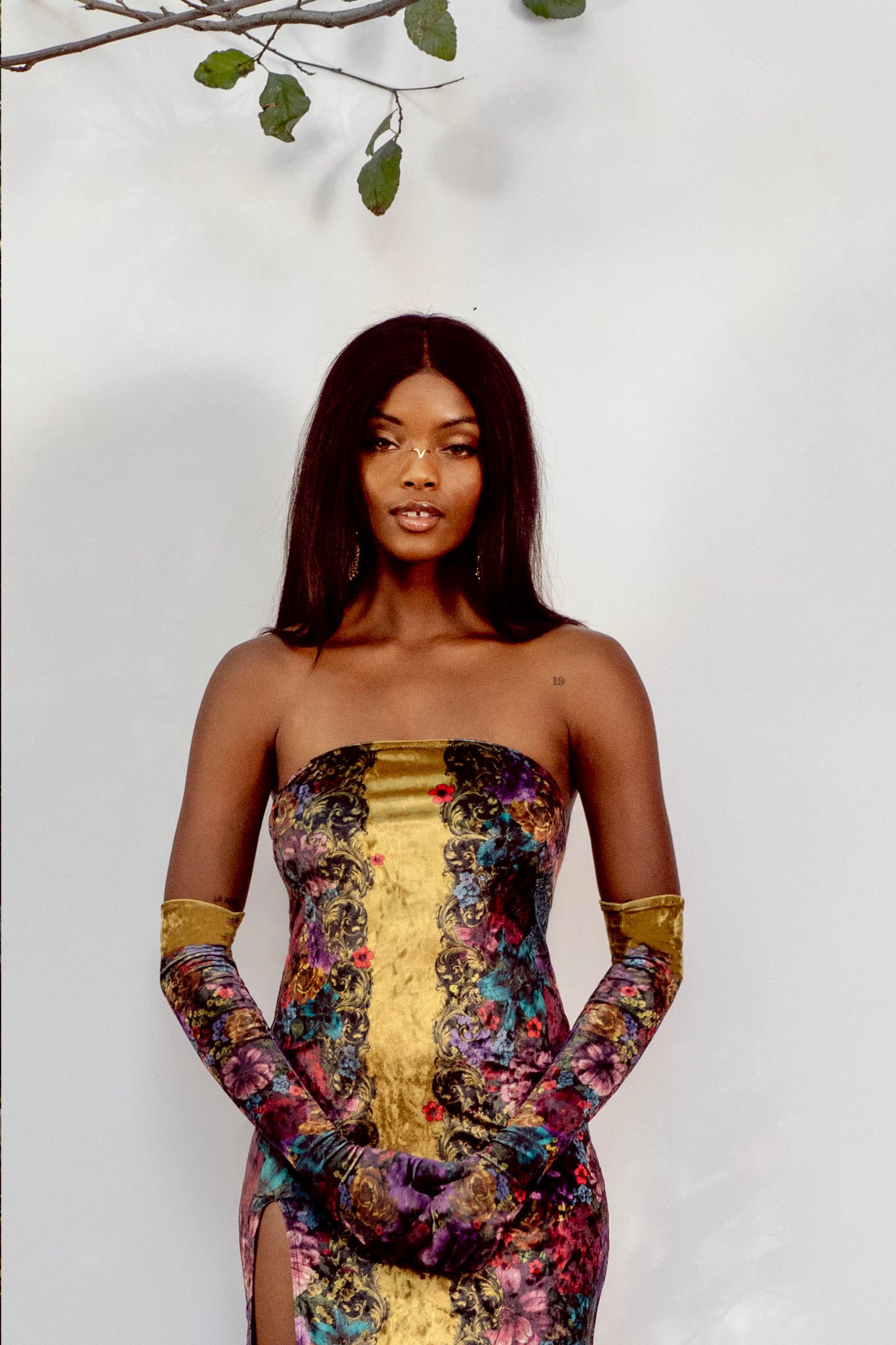 Woman wearing a colorful strapless dress with gold accents against a white background