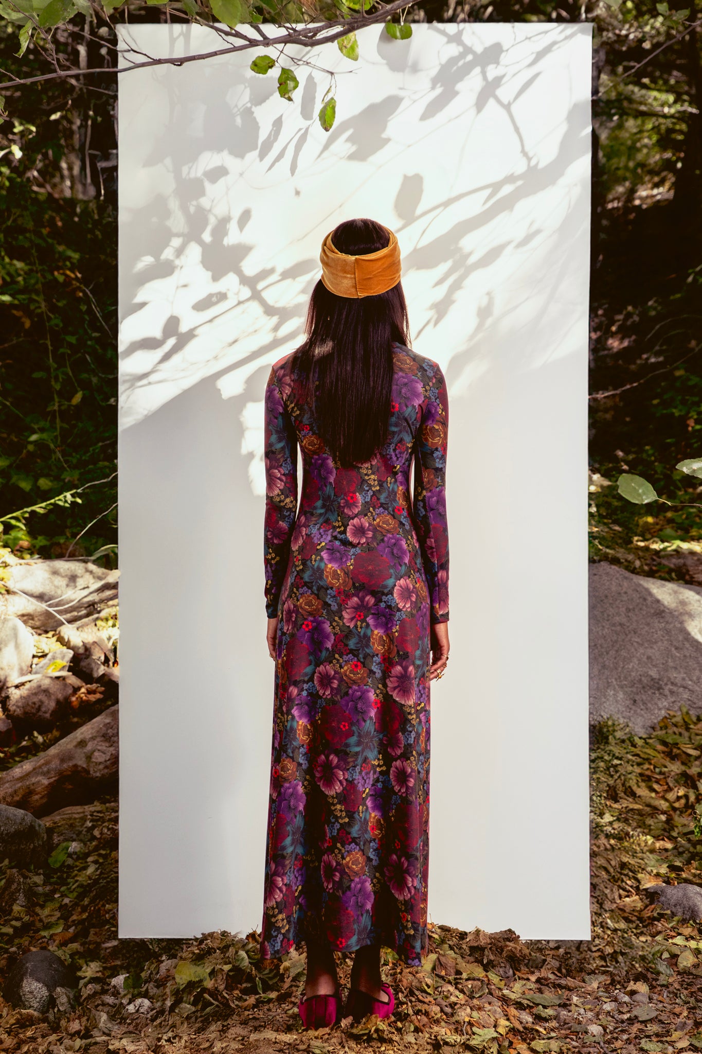 Woman in a colorful floral dress standing against a white background with natural elements around.