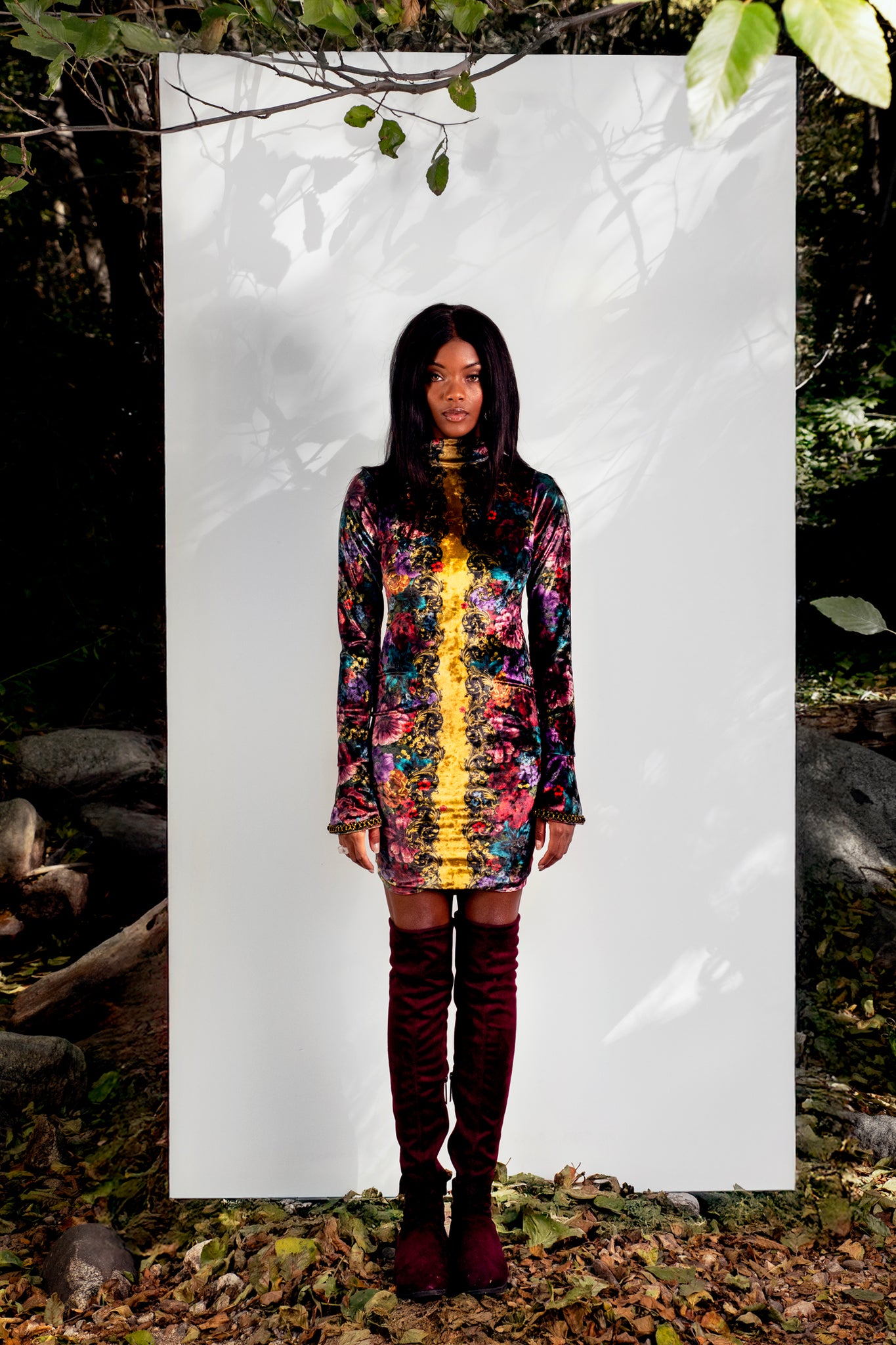 Woman in a colorful mini dress standing in front of a white panel with nature in the background