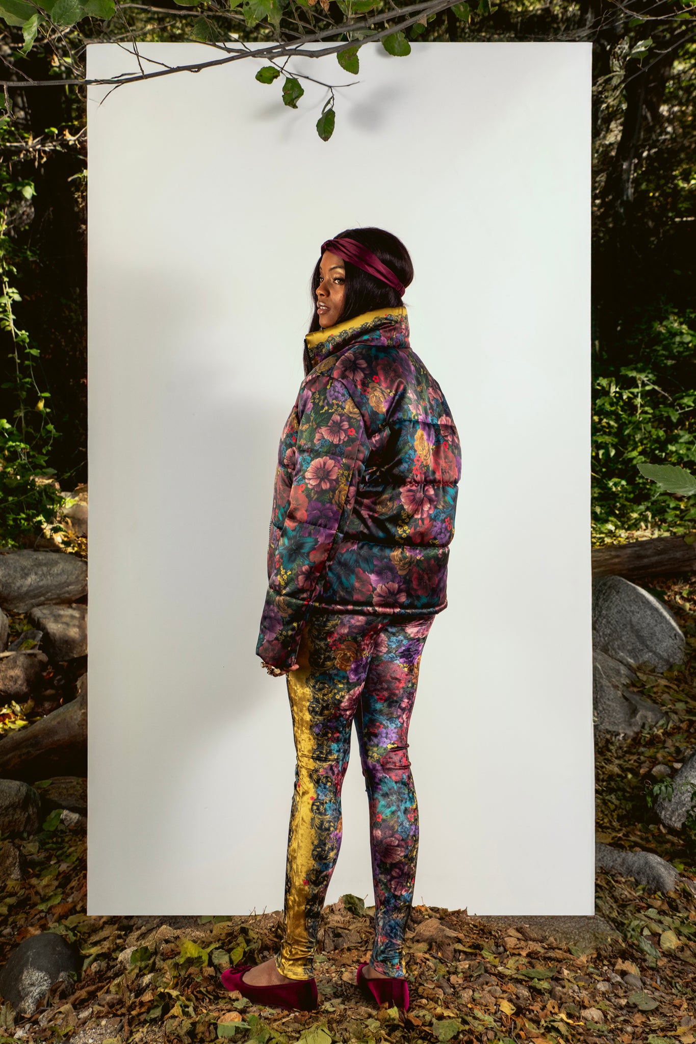 Person wearing a floral puffer standing against a white background with a natural setting.