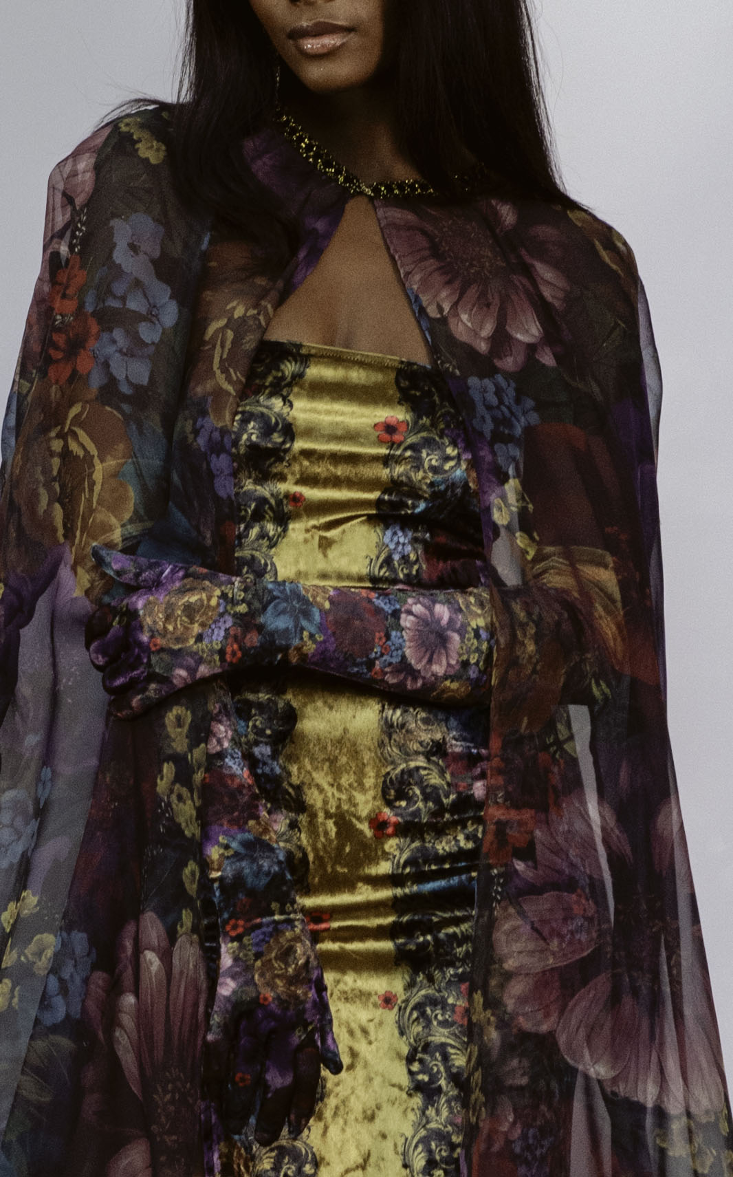 Woman wearing a gold dress with a floral shawl over a white background