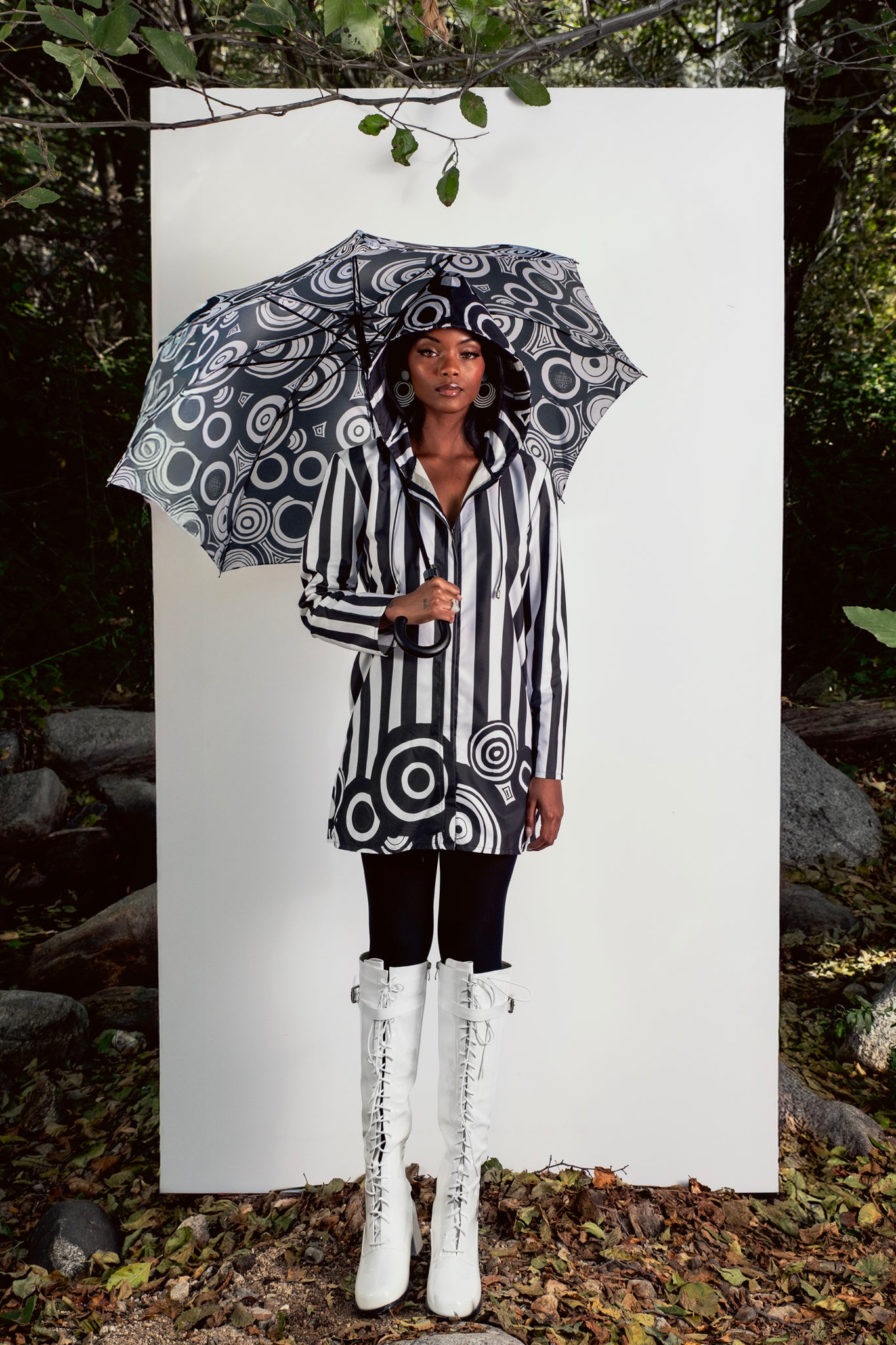 Person wearing a black and white patterned raincoat with a matching umbrella outdoors.