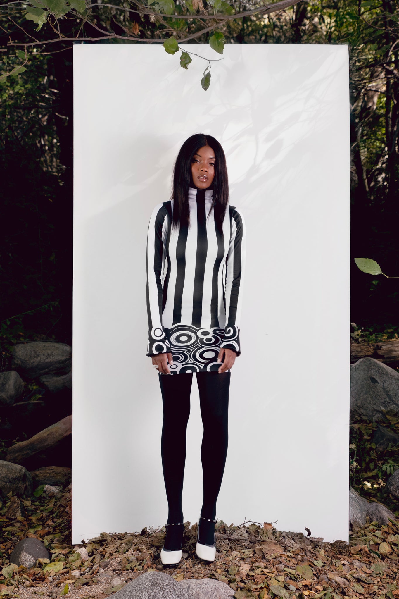 Person wearing a black and white mini dress standing against a white backdrop outdoors.