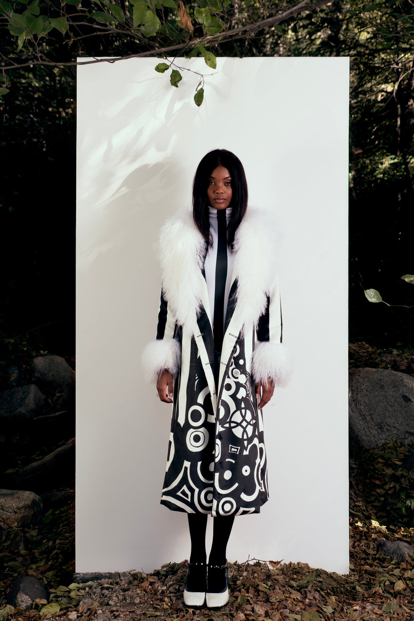 Person wearing a long, patterned coat with white fur trim against a natural background